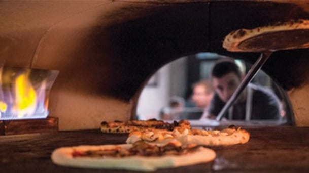 pizza being cooked inside of a wood fire grill with the chef placing another pizza in the oven