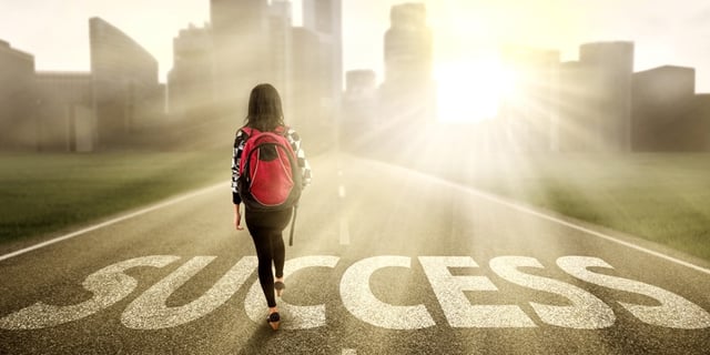 Girl wearing a bookbag walking across the word "success" painted on a road. 