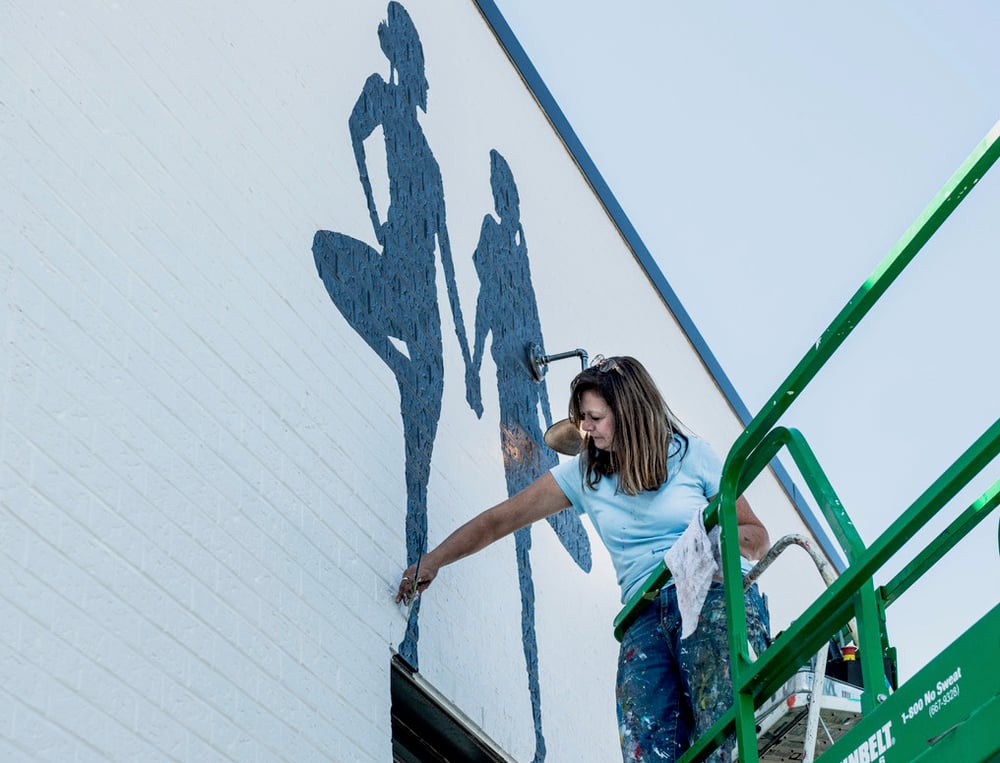 Lisa Gaither painting a mural of women holding hands