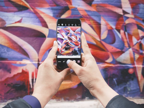 hands holding phone taking picture of a purple and red colored mural