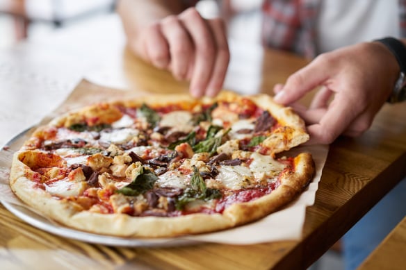 A man taking a slice from a pizza pie. 