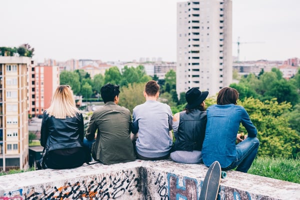 Five young people sitting on a wall outside with their backs to the camera. 