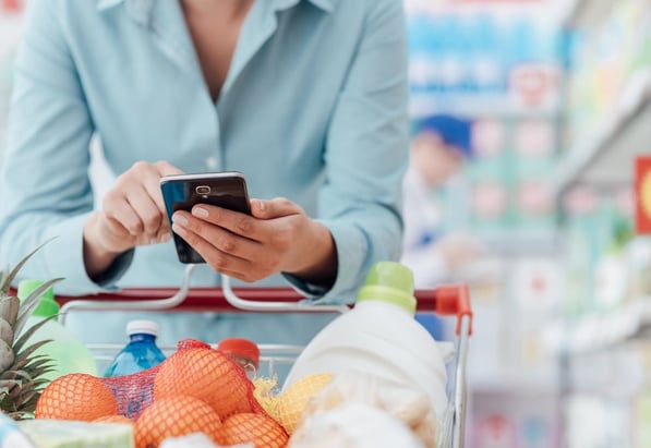 Woman with a full shopping cart searching on her phone.  